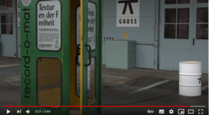 Screenshot aus Videoprojekt "Texturen der Freiheit". Zu sehen ist eine grüne Telefonzelle mit einem Thalia Plakat an der Scheibe, deren Tür leicht geöffnet steht.